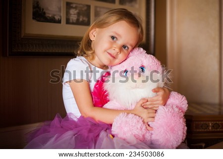 beautiful  smiling  little blonde girl  in pink skirt with soft toy  on home background birthday