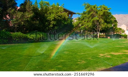 beautiful landscape with automatic  sprinkler spraying  watering the lawn in the home garden with a rainbow in water drops