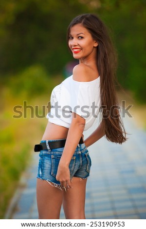 beautiful  brunette  sexy  smiling  woman in blue jeans shorts and white shirt go green park  has long hair and elegant tan body