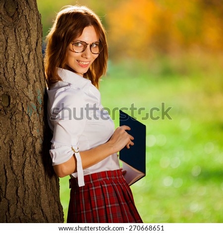 beautiful  smiling red haired woman white blouse, red skirt, glasses and book posing autumn yellow  nature background outdoor holiday