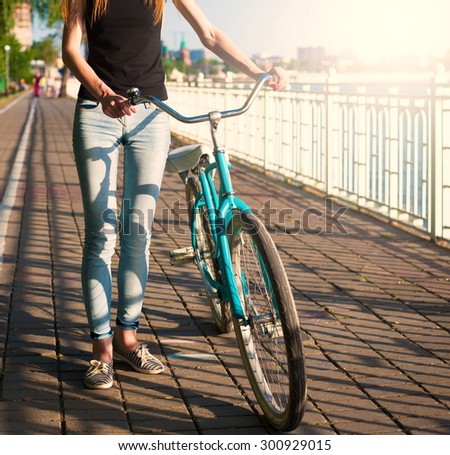 Beautiful sensuality elegance brown hair woman cyclist, has black shirt, blue jeans. Has slim sport body. Motion on great bicycle in urban city.