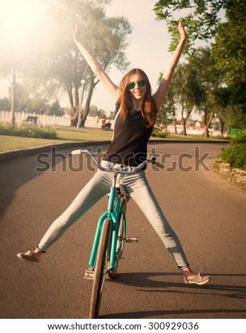 Beautiful sensuality elegance brown hair woman cyclist, has happy fun cheerful smiling face, black shirt, blue jeans. Has slim sport body. Motion on great bicycle in urban city. Portrait nature.