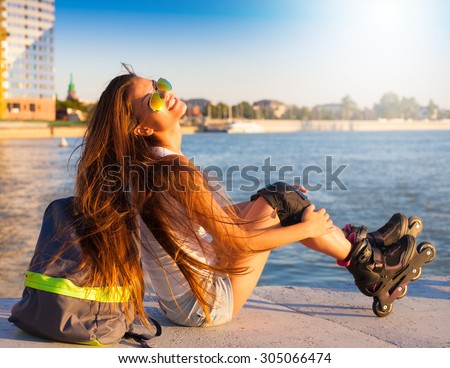 Beautiful sensuality elegance brunette woman, has happy fun cheerful smiling face, white shirt, blue jeans shorts. Has slim sport tan body. Motion on great rollerblading urban city. Portrait nature.
