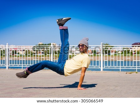 Fun man dancing. Has yellow t-shirt, blue jeans, gray shoes sneakers, slim sport body. Motion on great urban city. Amazing portrait. Sports acrobatic handstand. Fitness concept. Cool jump.