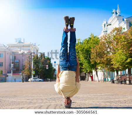 Fun man dancing. Has yellow t-shirt, blue jeans, gray shoes sneakers, slim sport body. Motion on great urban city. Amazing portrait. Sports acrobatic handstand. Fitness concept. Cool jump.