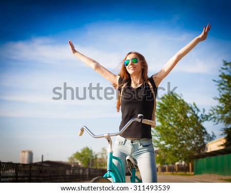 Beautiful sensuality elegance brown hair woman cyclist, has happy fun cheerful smiling face, black shirt, blue jeans. Has slim sport body. Motion on great bicycle in urban city. Portrait nature.