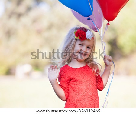 Beautiful little blonde girl, has happy fun cheerful smiling face, red dress, multicolored balloons. Portrait nature.