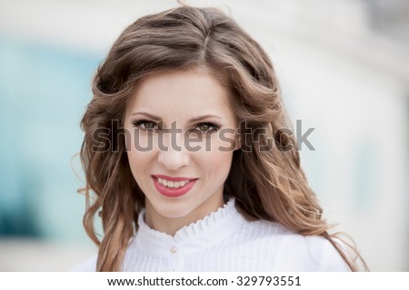 Beautiful young romantic elegant woman face, has brown eyes, haired nature ringlets hair, sexy red lips, white teeth, happy fun smile. Pure makeup. White background. Bright day.