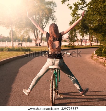Beautiful sensuality elegance red hair back woman cyclist, has black shirt, blue jeans. Has slim sport body and ass. Motion on great bicycle in urban city. Portrait nature amazing sunset.