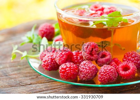 Beautiful green tea with raspberries and mint. Garden fruit background. Sunny day. Lifestyle medicine.