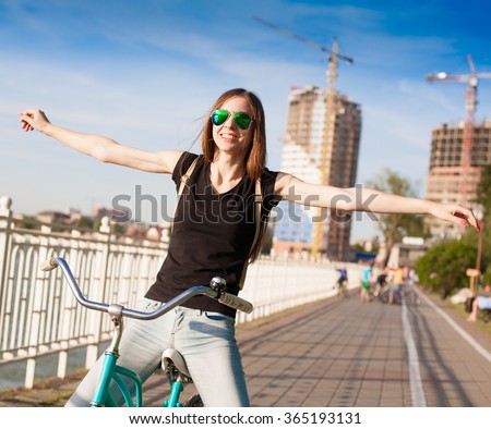 Beautiful sensuality elegance brown hair woman cyclist, has happy fun cheerful smiling face, black t-shirt, blue jeans. Has slim sport body. Motion on great bicycle in urban city. Portrait nature.