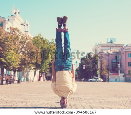 Fun man dancing. Has yellow t-shirt, blue jeans, slim sport body. Motion on great urban city. Amazing portrait. Sports acrobatic handstand. Fitness concept. Cool jump. Head over heels.