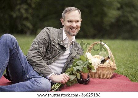man by picnic holding flowers and laughs in a city park
