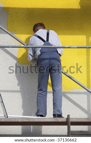 man on a scaffold painting houser with roller