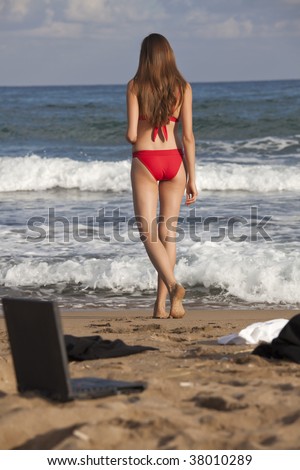 woman in bikinis standing at the beach - laptop, jacket and blouse lying in sand