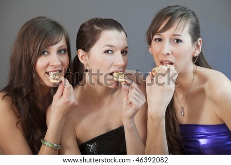 three women eating small pizzas over grey background