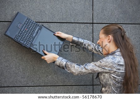 angry woman smashing a laptop computer against the wall