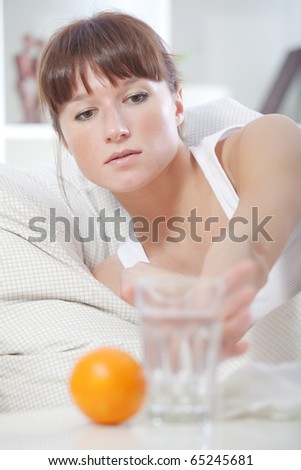 sick woman in bed reaching for glass water on table