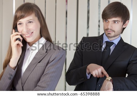 business woman talking on phone - frustrated businessman pointing on his watch. Focus on man