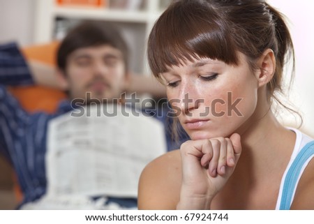 sad woman in front of sleeping man with newspaper