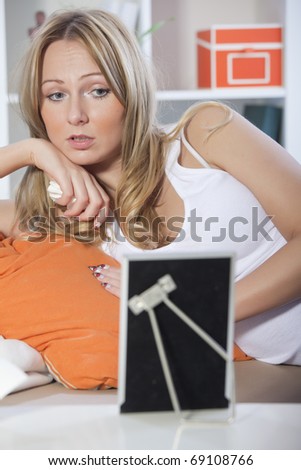 Sad blond woman sitting on couch, looking at a framed picture