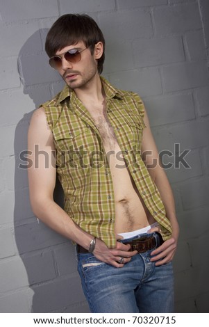 cool man in sunglasses and open shirt standing at the brick wall