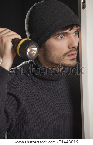 burglar with pocket lamp looking into the room
