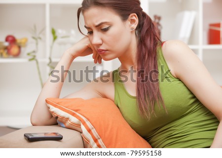 young woman sitting on sofa and looking at phone, waiting for the call