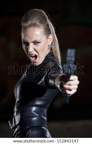 angry and screaming woman in leather suit aiming with a gun