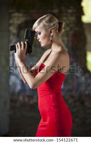 Gun woman in red dress in vintage look posing in old fabric ruins
