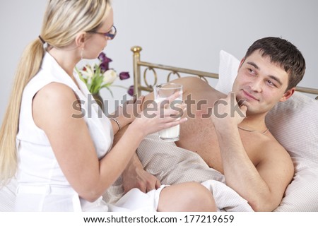 Woman with glass milk and sick man on bed