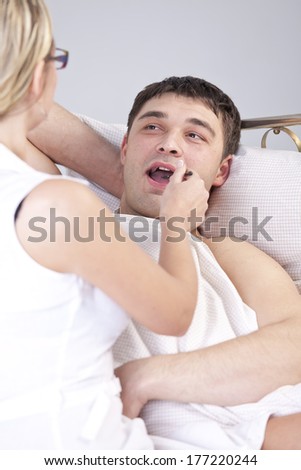 Female doctor examining male tongue on the bed