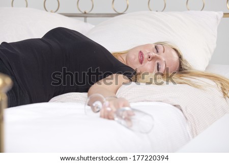 Drunk woman in black shirt with glass, sleeping in bed