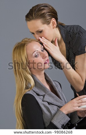 Woman telling a secret to another - gossip over a grey background