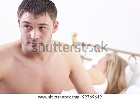 worried man sitting on bed - woman sleeping in background