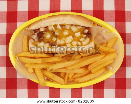 Hot dog in a bun with chili, melted cheddar cheese, and diced onions, served in a basket with french fries.
