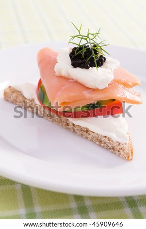 Smoked salmon canape on rye bread with cream cheese, red bell pepper, cucumber, black caviar, and fresh dill.