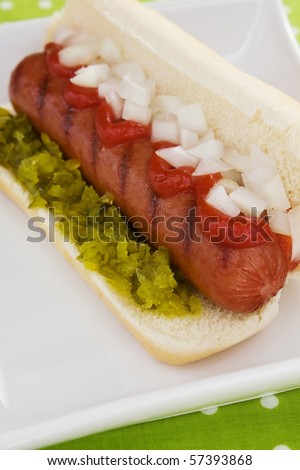 A plump beef hot dog on a bun topped with sweet pickle relish, diced onions, and ketchup.
