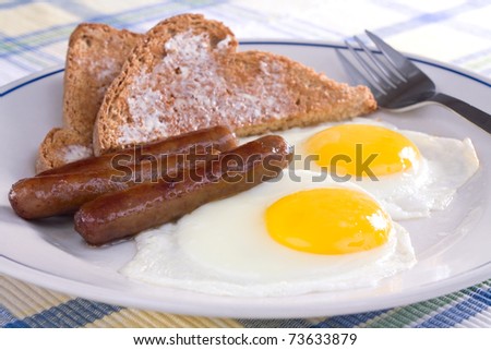 Fried sunny side up eggs with sausage links and buttered wheat toast.