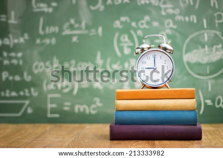 school books with alarm clock on green school board background
