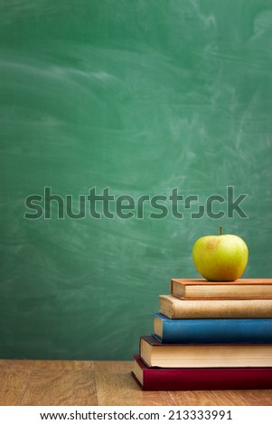 School books with apple on desk over green  school board background