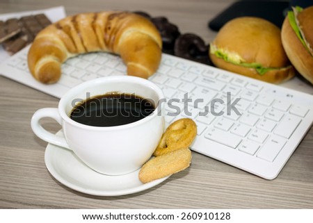 Cup of coffee and chocolate biscuits desk with computer, bad habit of constant snacking during work