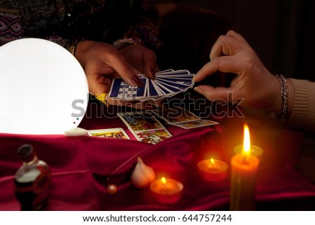 Woman fortune teller holding tarot cards in her hands and another woman picking the card