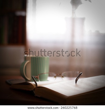 cup with book on a table and shelf with books next to window on background
