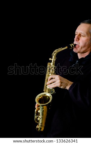 A Musician dressed in black is playing jazz music on his golden saxophone in front of a black background
