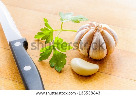 A clove of garlic and some leaves of parsley, with a knife