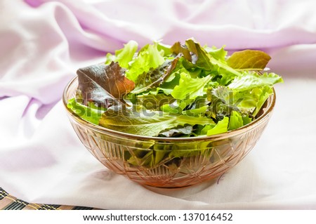 Mixed green and red salad in a bowl, with a pink tablecloth