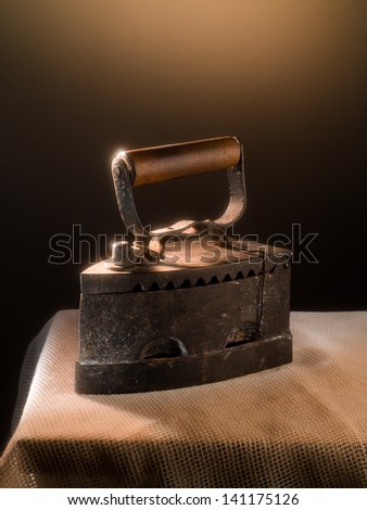 A old rusted smoothing iron with a wooden handle working with carbon stands on a table with burlap