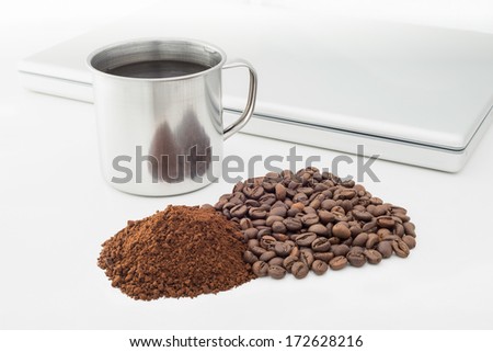 A warm metallic cup of coffee with coffee beans, instant soluble coffee and laptop computer