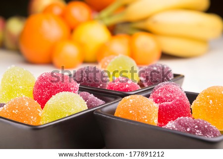 Colorful fruit jelly in little black ceramic cups. Fruits in the background